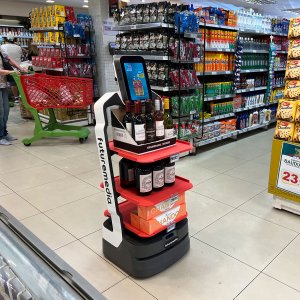 Robô Nik trabalhando em supermercado em modo promocional expondo bebidas em suas bandejas