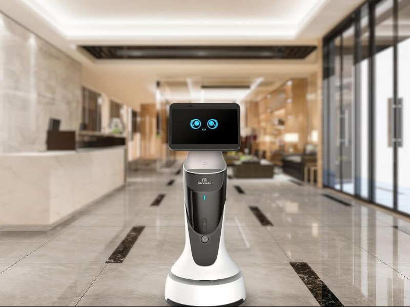 Robô Buddy com rosto sorridente na tela, trabalhando próximo à recepção Robô Buddy com rosto sorridente na tela, trabalhando próximo à recepção